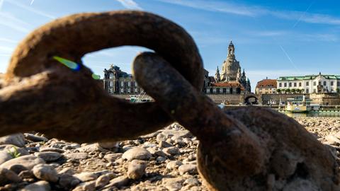 Durch eine verrostete Schiffskette kann der Blick über den Fluss schweifen, an dem das historische Dresden mit seiner Frauenkirche liegt.