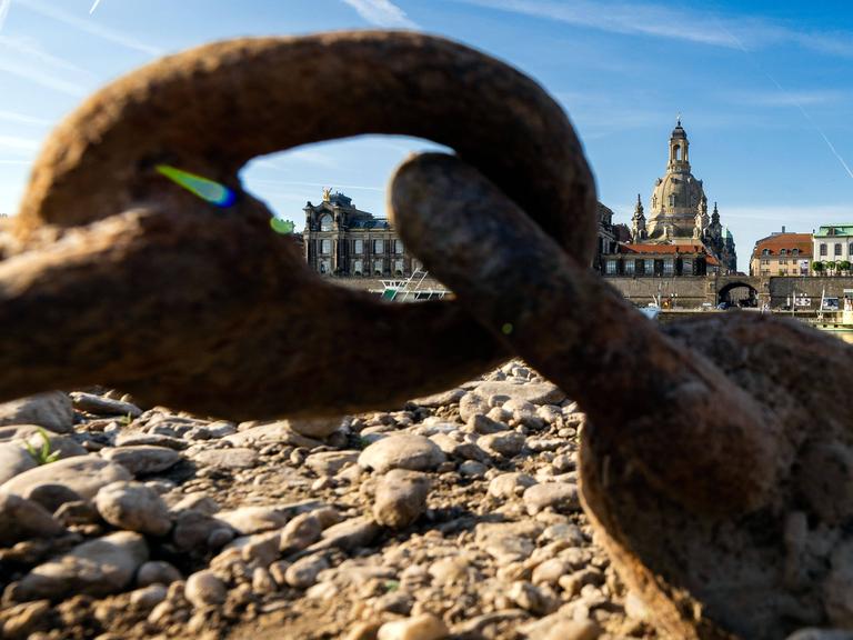 Durch eine verrostete Schiffskette kann der Blick über den Fluss schweifen, an dem das historische Dresden mit seiner Frauenkirche liegt.