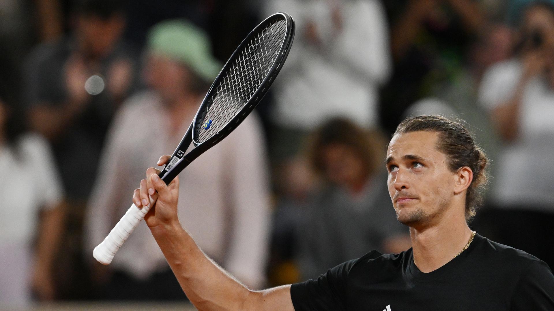 Tennisspieler Alexander Zverev hebt mit der rechten Hand seinen Schläger und lächelt. Tennisspieler Alexander Zverev hebt mit der rechten Hand seinen Schläger und lächelt.