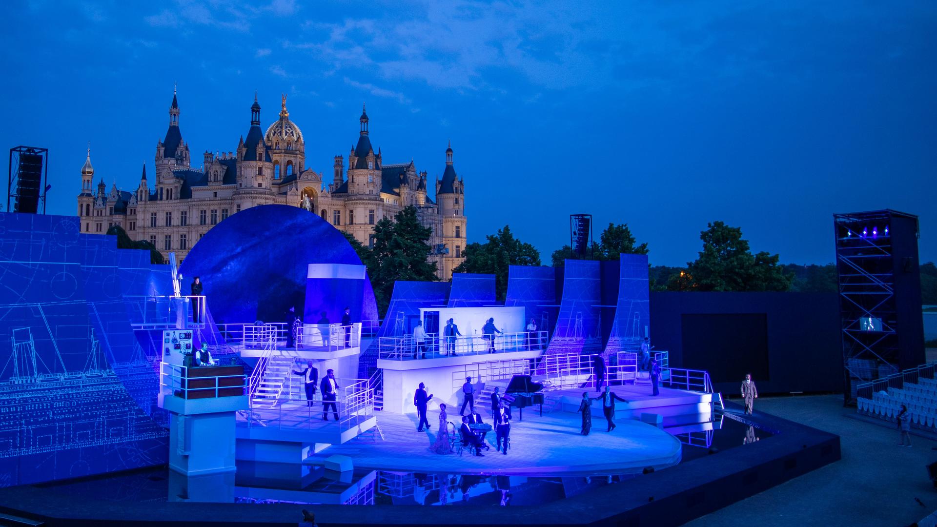Sänger und Schauspieler spiegeln sich im Musical "Titanic" auf der Bühne der Schlossfestspiele Schwerin in einer Wasserfläche.