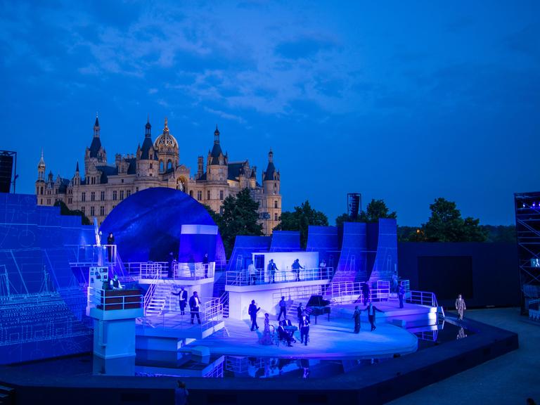 Sänger und Schauspieler spiegeln sich im Musical "Titanic" auf der Bühne der Schlossfestspiele Schwerin in einer Wasserfläche.