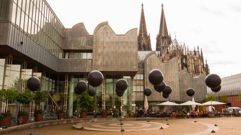 Vor der Kulisse von Philharmonie und Kölner Dom schweben sechzehn schwarze Ballons in der Luft, die eine musikalische Installation  darstellen.