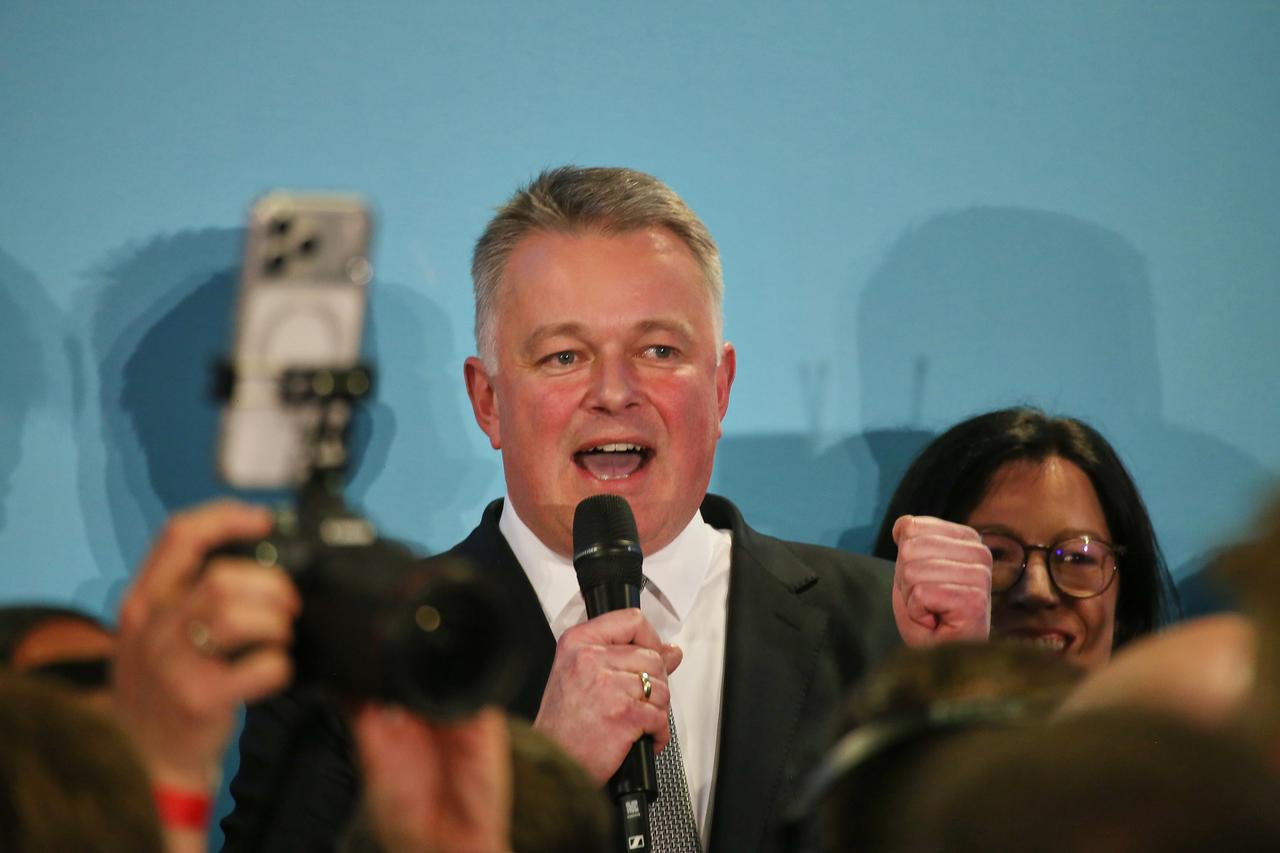 Gordon Schnieder steht vor einer türkisfarbenen Wand und spricht in ein Mikrofon. Er ballt die linke Faust und lächelt. Gordon Schnieder steht vor einer türkisfarbenen Wand und spricht in ein Mikrofon. Er ballt die linke Faust und lächelt.