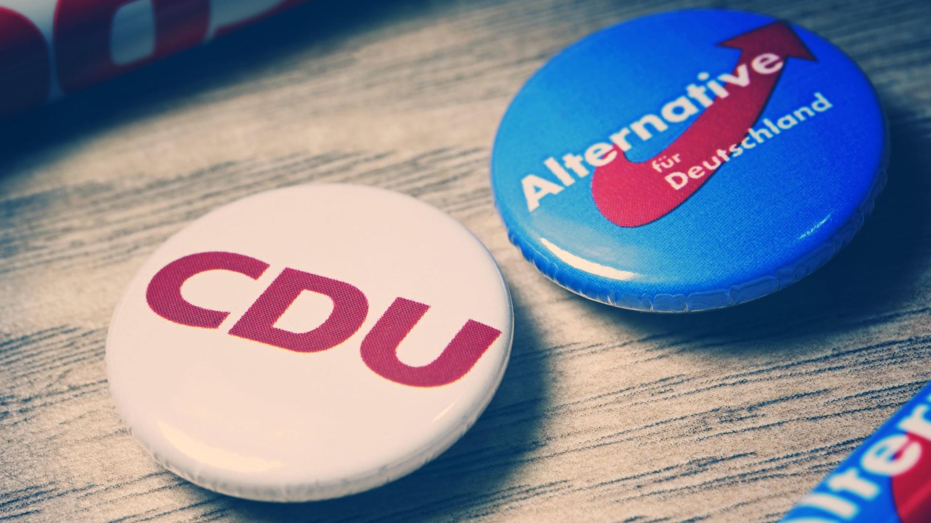 Partei-Anstecker mit Logos von CDU und AfD liegen auf einer Holzplatte Partei-Anstecker mit Logos von CDU und AfD liegen auf einer Holzplatte