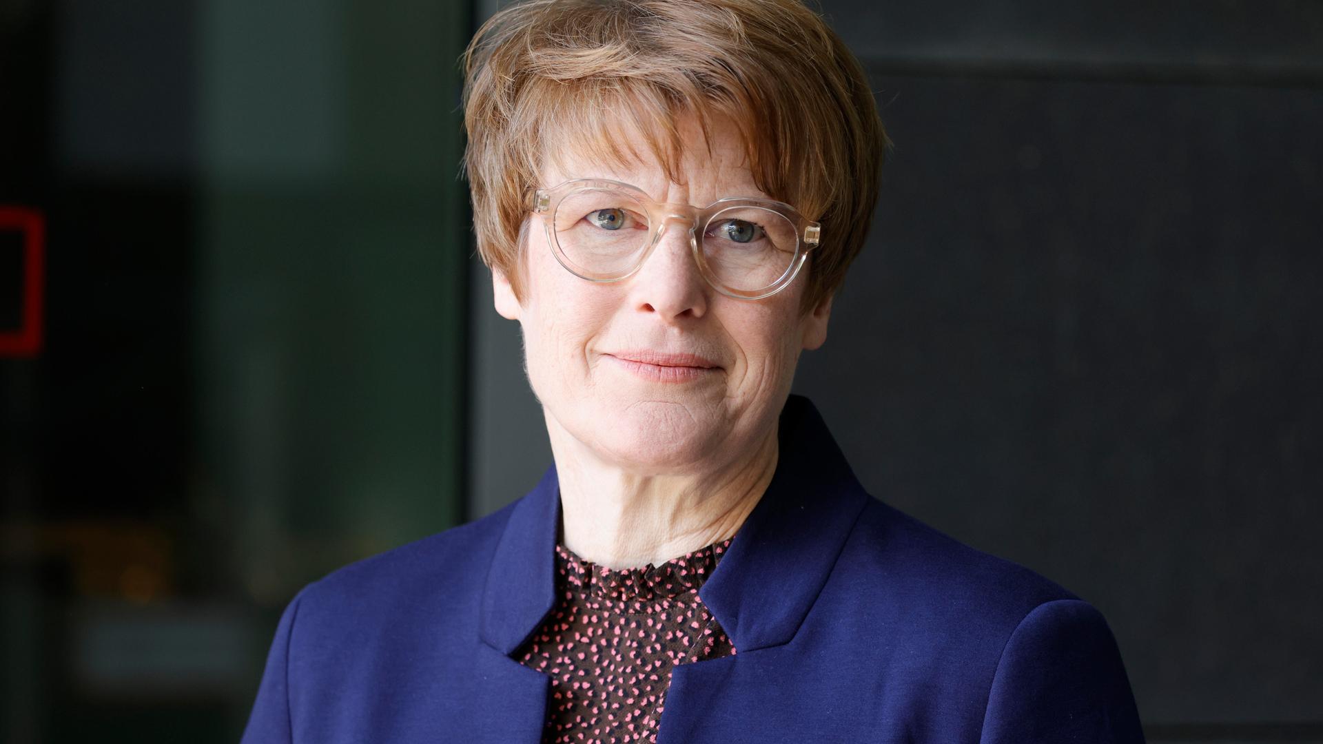 Veronika Grimm trägt eine hell umrandete Brille, ein dunkelblaues Sakko und schaut freundlich in die Kamera. Veronika Grimm trägt eine hell umrandete Brille, ein dunkelblaues Sakko und schaut freundlich in die Kamera.