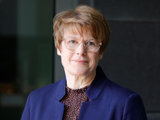 Veronika Grimm trägt eine hell umrandete Brille, ein dunkelblaues Sakko und schaut freundlich in die Kamera.