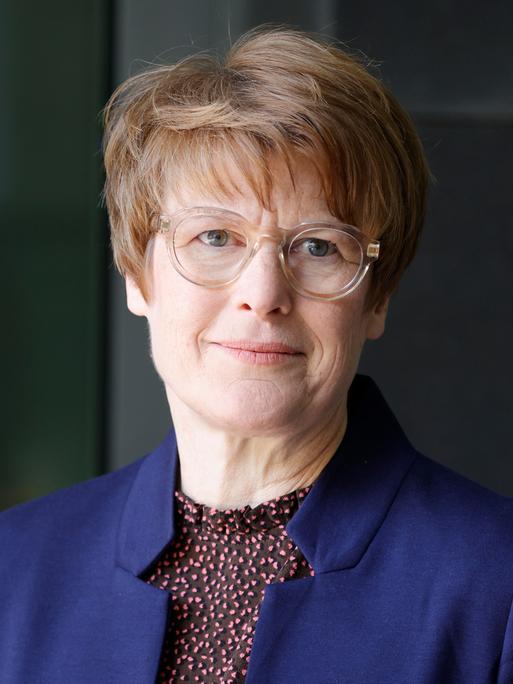 Veronika Grimm trägt eine hell umrandete Brille, ein dunkelblaues Sakko und schaut freundlich in die Kamera.