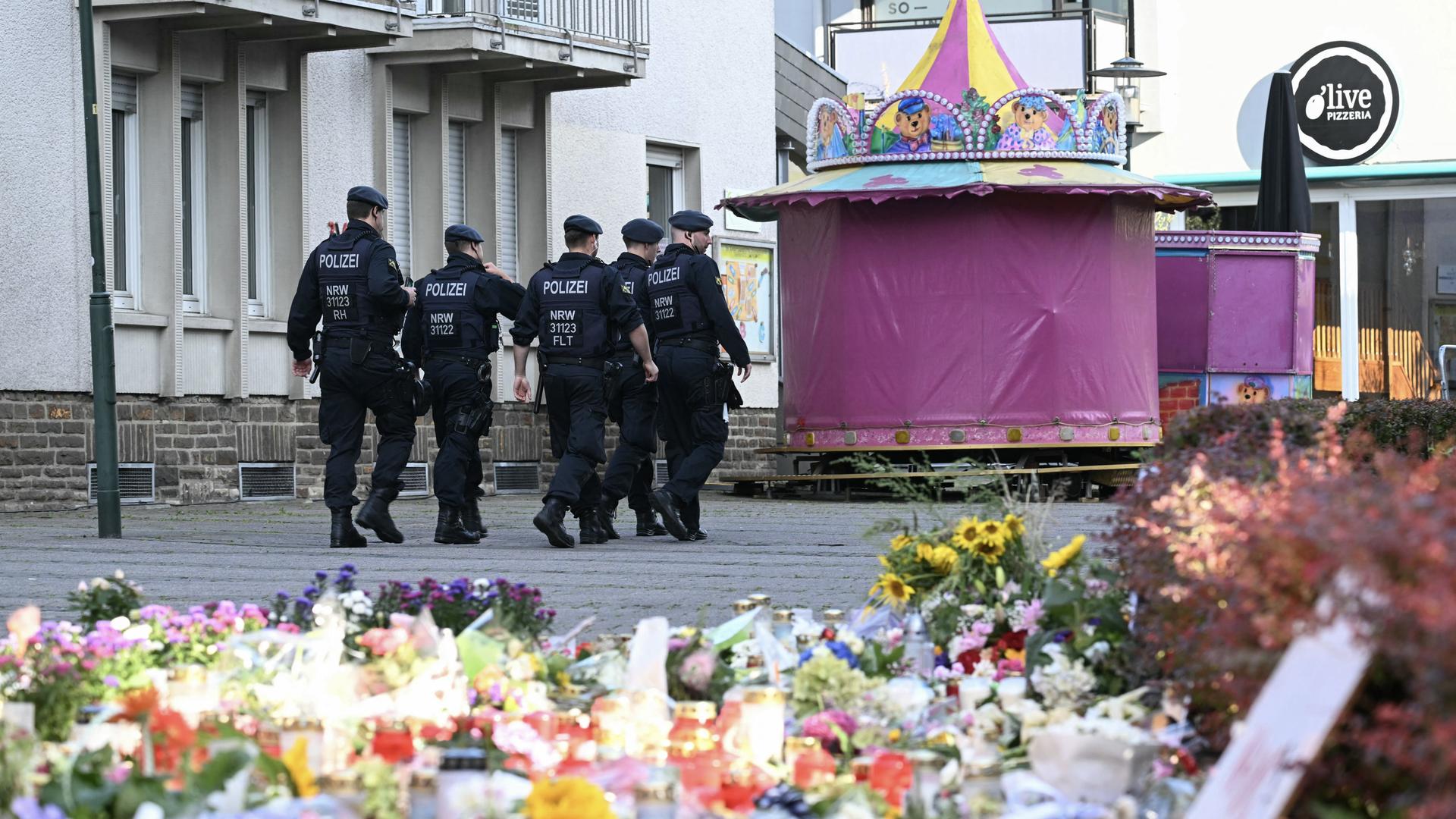 Polizisten patrouillieren in der Nähe des Tatorts in Solingen. Im Bildvordergrund sind abgelegte Blumen zu sehen.