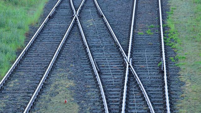 Bahngleise mit Weiche auf schwarzen Schotter, dazwischen wächst teilweise Gras