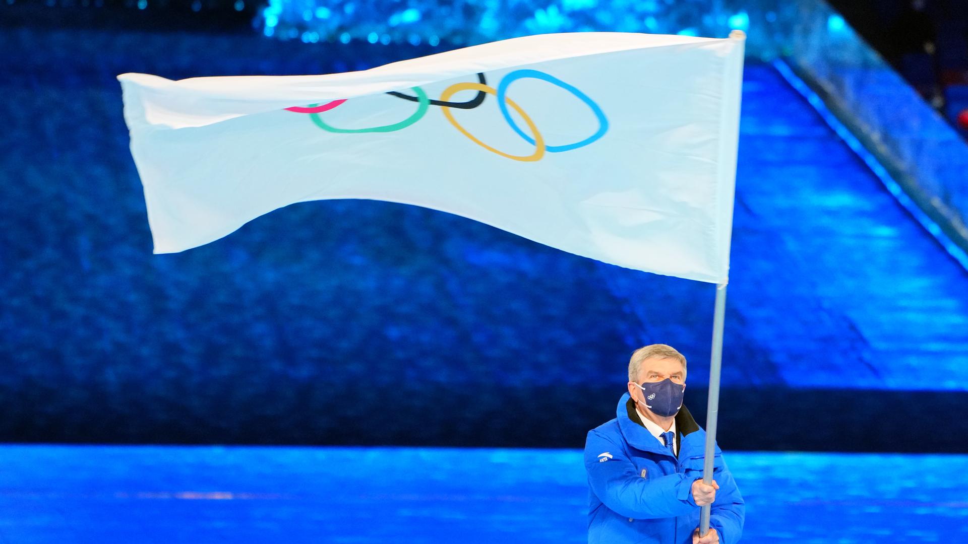 Thomas Bach, Präsident des IOC, schwenkt bei der Abschlussfeier in Peking die Olympische Flagge.