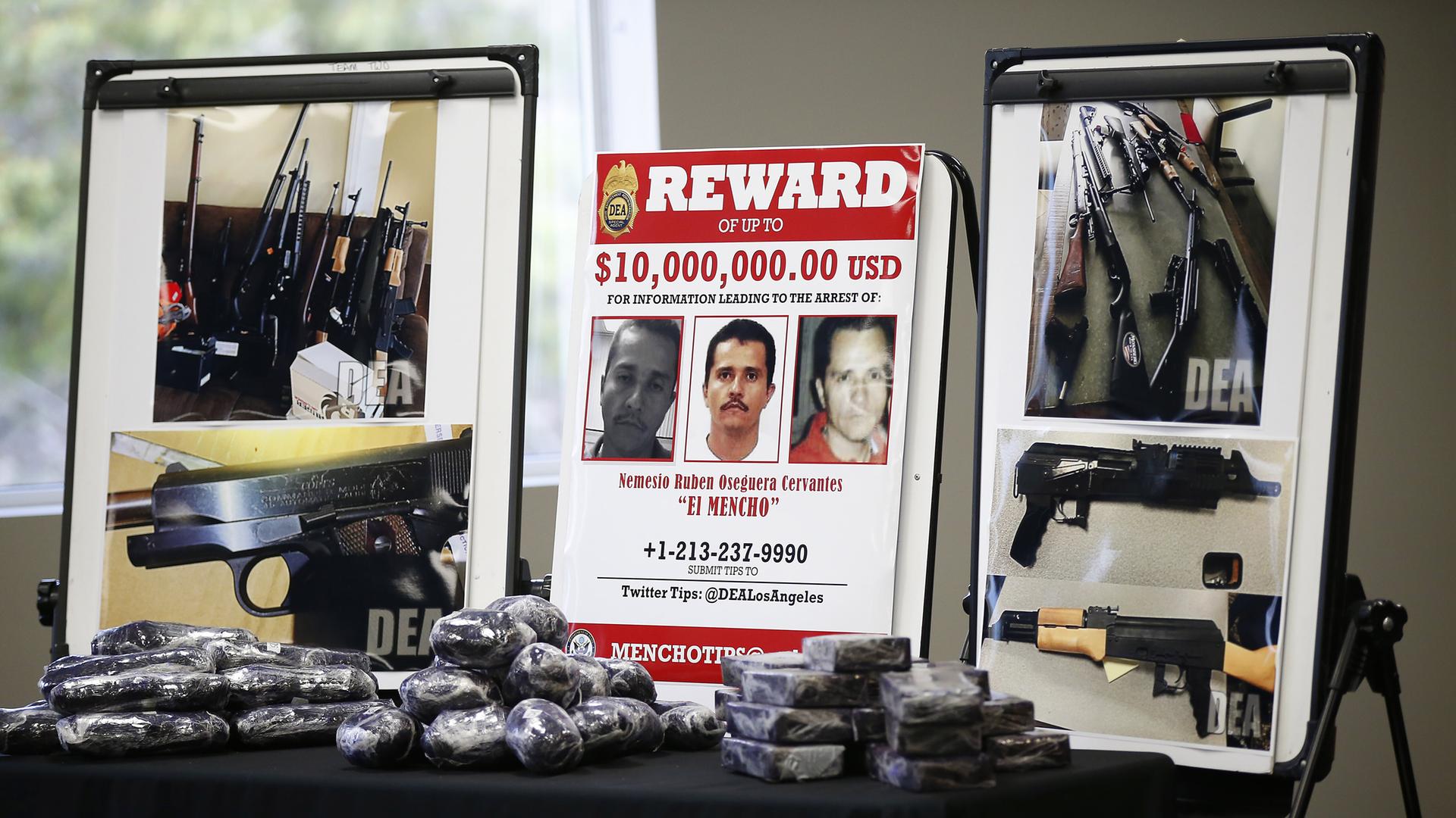 Es zeigt ein Fahndungsfoto des mexikanischen Drogenkartellboss Cervantes, auf den ein Kopfgeld von 10 Millionen US-Dollar ausgesetzt war. Daneben sind Fotos von Schusswaffen zu sehen. Vor den aufgestellten Bildern liegen schwarz-verpackte Päckchen. Es zeigt ein Fahndungsfoto des mexikanischen Drogenkartellboss Cervantes, auf den ein Kopfgeld von 10 Millionen US-Dollar ausgesetzt war. Daneben sind Fotos von Schusswaffen zu sehen. Vor den aufgestellten Bildern liegen schwarz-verpackte Päckchen.