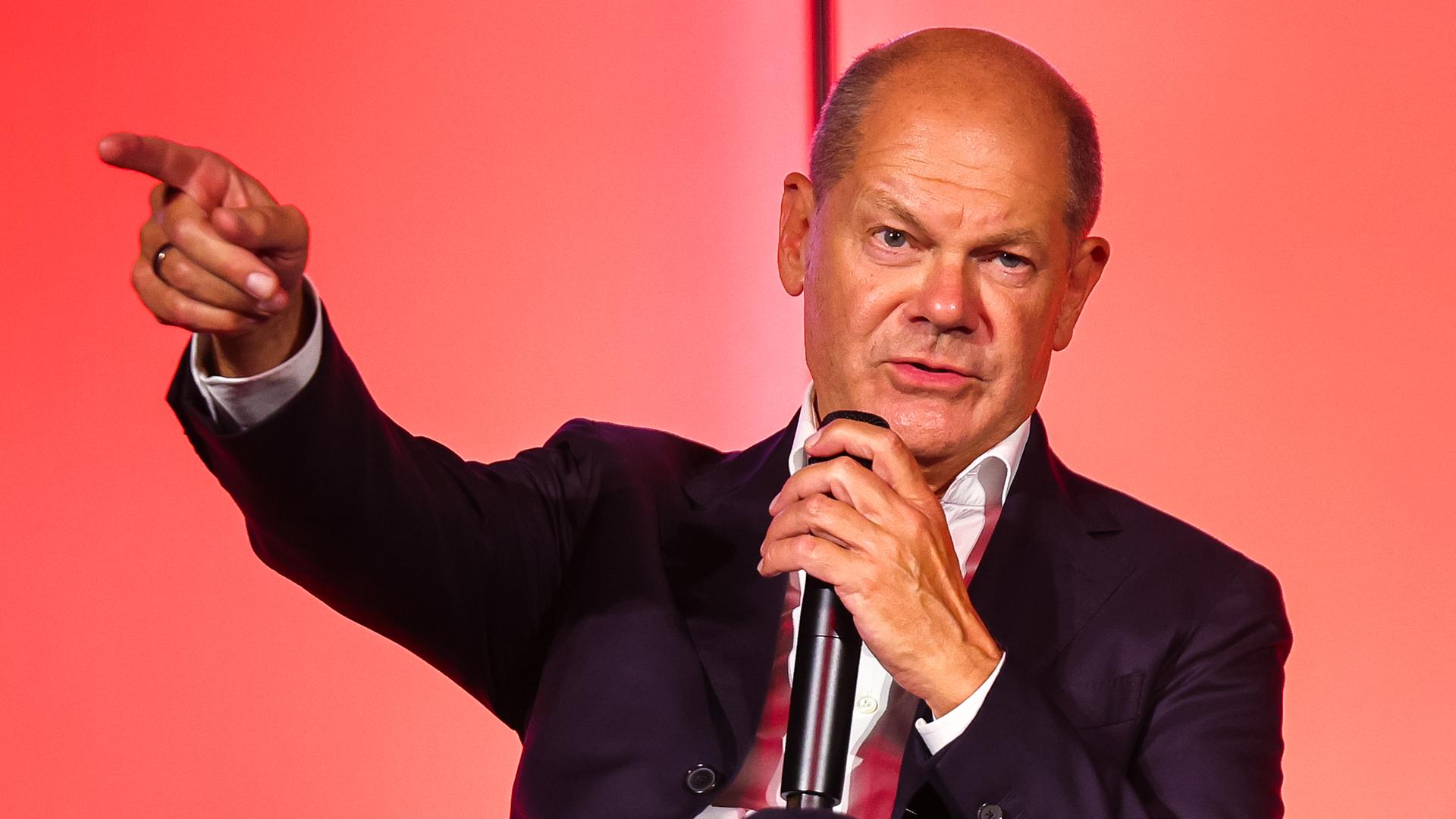 Bundeskanzler Scholz mit ausgestrecker Hand beim Sprechen in ein Mikrofon 