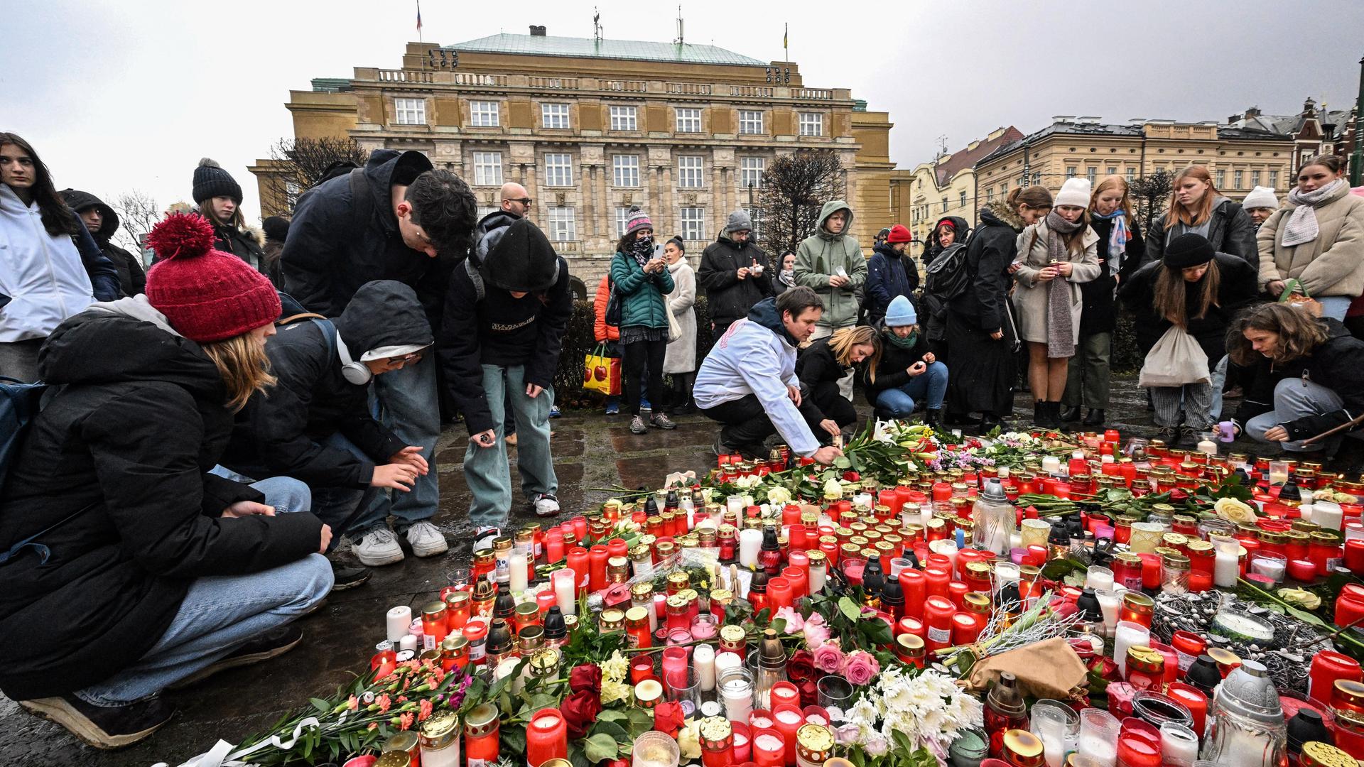 Menschen legen Blumen auf den Gehweg und stellen Kerzen auf. Im Hintergrund ist die Karls-Univerisät von Prag zu sehen.