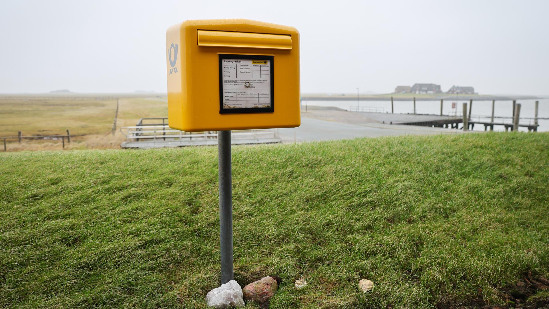 Ein Briefkasten der Deutschen Post mit Tide-abhängigen Leerungszeiten steht auf einer Warft auf der Hallig Langeneß.