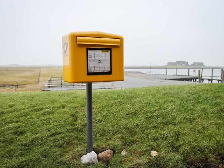 Ein Briefkasten der Deutschen Post mit Tide-abhängigen Leerungszeiten steht auf einer Warft auf der Hallig Langeneß.