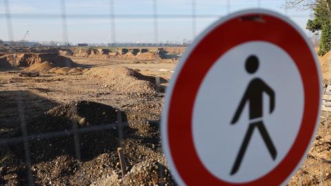 Das Verkehrsschild "Verbot für Fußgänger" hängt an einem Bauzaum, hinter dem eine gigantische Sandlandschaft zu sehen ist.