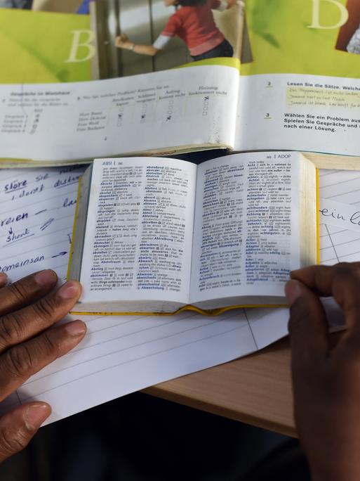 Eine Person nimmt an einem "Integrationskurs Deutsch" teil und hat vor sich Lehr- und Wörterbuch sowie ein Heft liegen. Eine Person nimmt an einem "Integrationskurs Deutsch" teil und hat vor sich Lehr- und Wörterbuch sowie ein Heft liegen.