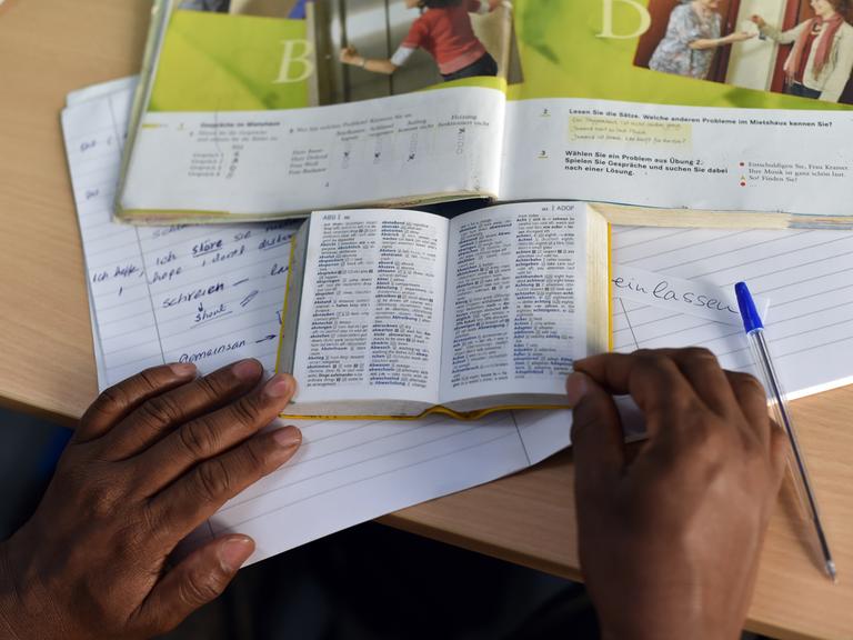 Eine Person nimmt an einem "Integrationskurs Deutsch" teil und hat vor sich Lehr- und Wörterbuch sowie ein Heft liegen. Eine Person nimmt an einem "Integrationskurs Deutsch" teil und hat vor sich Lehr- und Wörterbuch sowie ein Heft liegen.