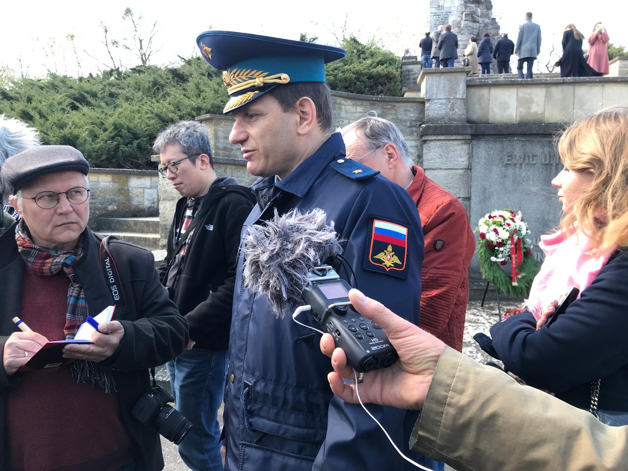 Ein russischer Militärattaché in Uniform an einem Gedenkort umringt von Journalisten