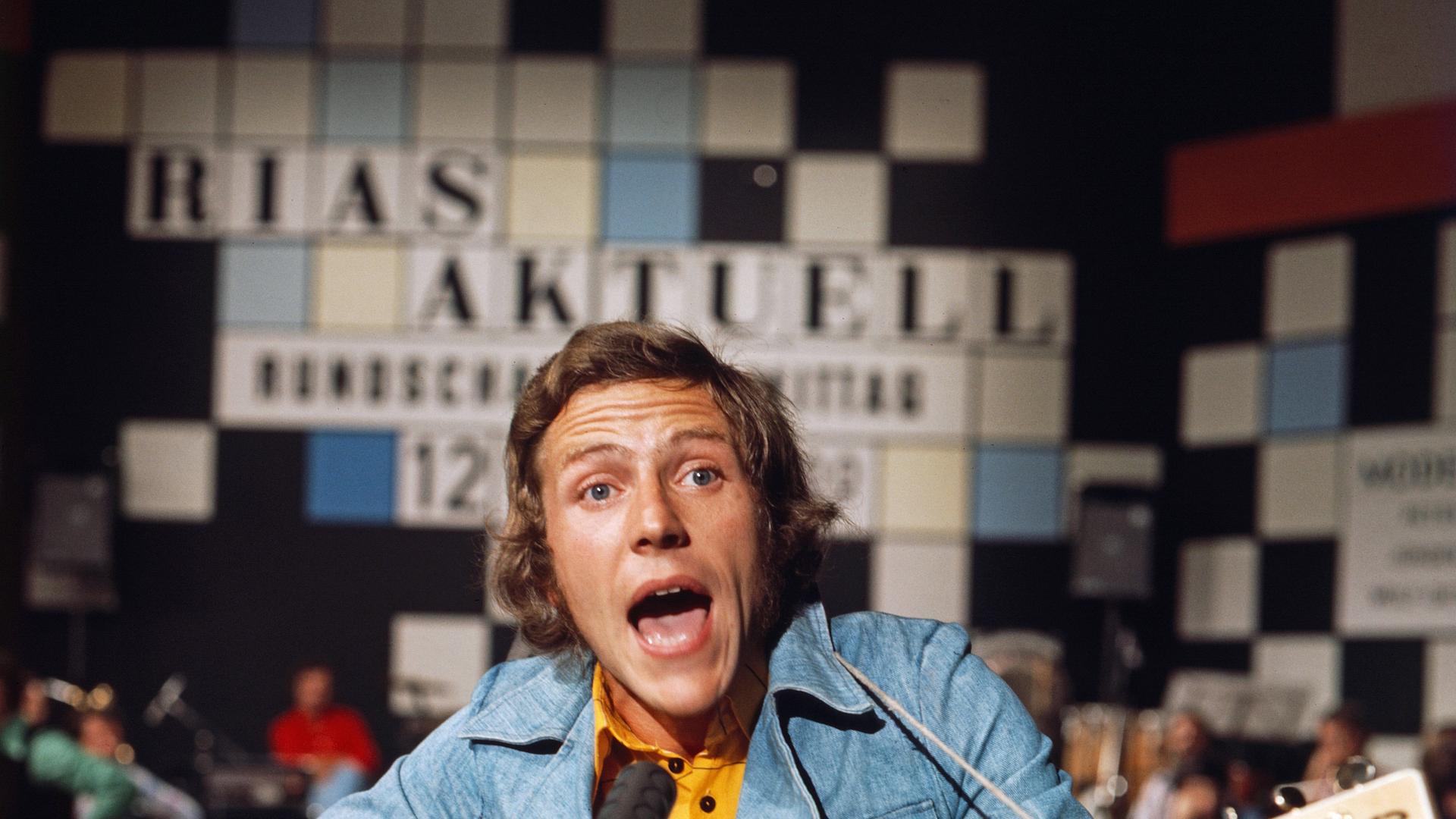 Michael Thilo singt in Jeansjacke, Im Hintergrund das Logo der Sendung "Rias aktuell". Michael Thilo singt in Jeansjacke, Im Hintergrund das Logo der Sendung "Rias aktuell".