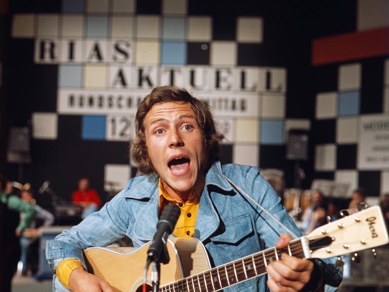 Michael Thilo singt in Jeansjacke, Im Hintergrund das Logo der Sendung "Rias aktuell". Michael Thilo singt in Jeansjacke, Im Hintergrund das Logo der Sendung "Rias aktuell".
