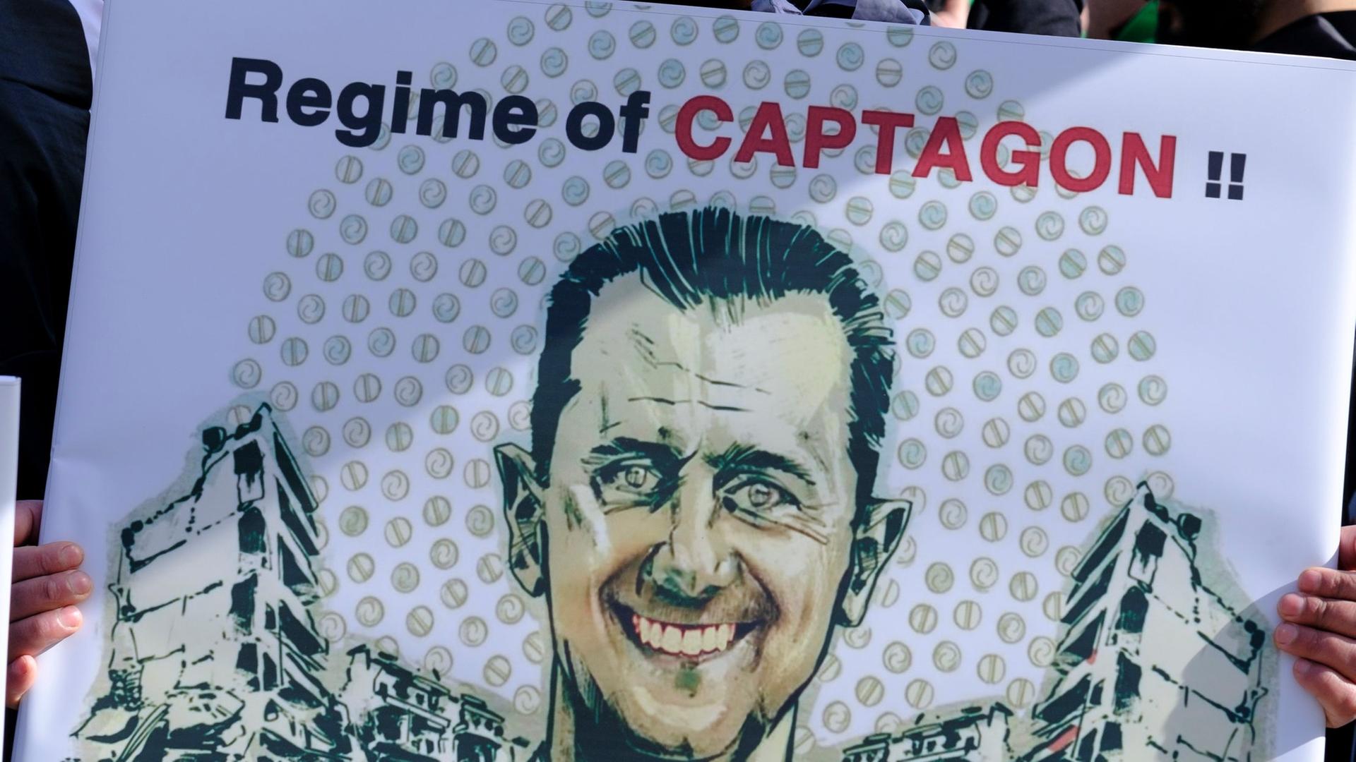 Ein Demonstrant hält ein Plakat mit dem Gesicht des syrischen Präsidenten Baschar al-Assad und der Aufschrift "Regime of Captagon".
