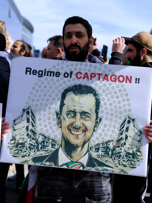 Ein Demonstrant hält ein Plakat mit dem Gesicht des syrischen Präsidenten Baschar al-Assad und der Aufschrift "Regime of Captagon".