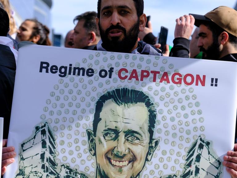 Ein Demonstrant hält ein Plakat mit dem Gesicht des syrischen Präsidenten Baschar al-Assad und der Aufschrift "Regime of Captagon".