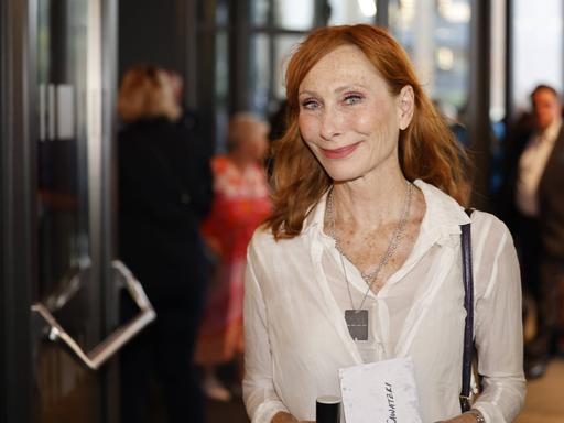 Andrea Sawatzki steht in der Lobby eines Gebäudes und lächelt freundlich in die Kamera