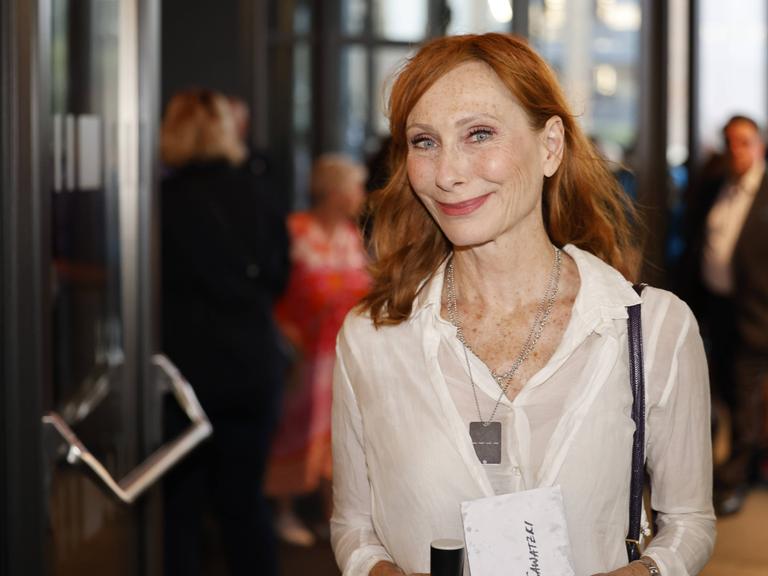 Andrea Sawatzki steht in der Lobby eines Gebäudes und lächelt freundlich in die Kamera