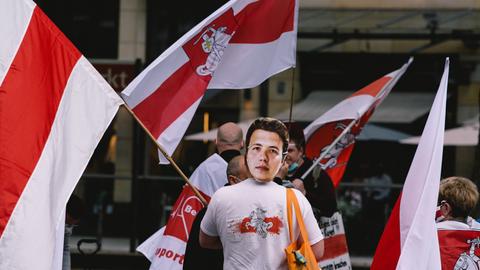 Verschiedene Menschen bei einer Demo mit den Flaggen von Belarus, einer trägt eine Maske von Roman Protassewitsch 