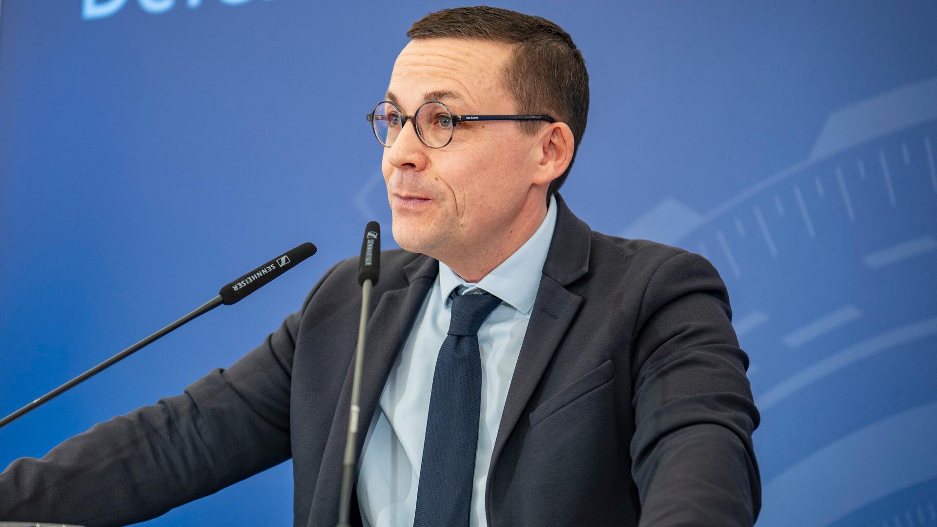 Roland Theis spricht bei einer Veranstaltung, er steht hinter zwei Mikrofonen. Roland Theis spricht bei einer Veranstaltung, er steht hinter zwei Mikrofonen.