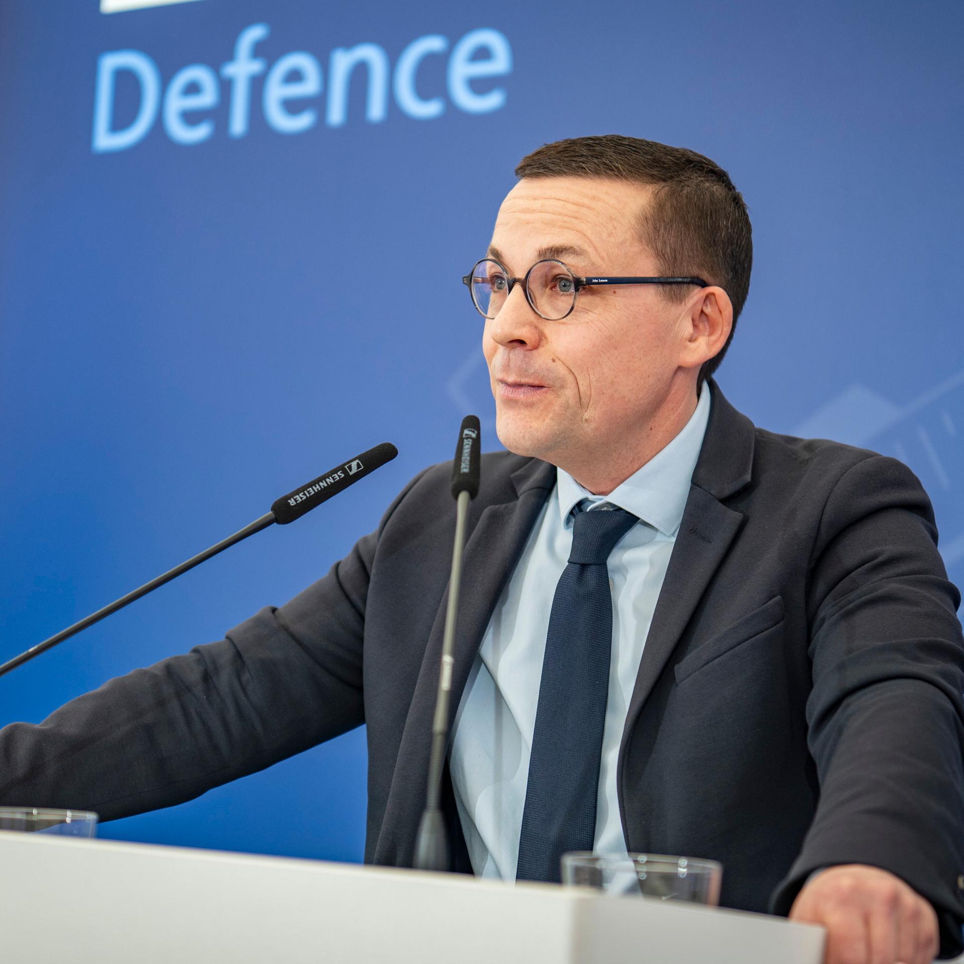 Roland Theis spricht bei einer Veranstaltung, er steht hinter zwei Mikrofonen.