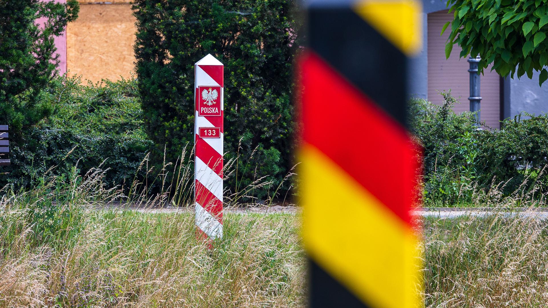 Grenzmarkierungen an der deutsch-polnischen Grenze. Im Vordergrund ein schwarz-rot-goldener Grenzpfosten der Bundesrepublik Deutschland, im Hintergrund ein rot-weisser Grenzpfosten mit dem Wappen der Republik Polen. Grenzmarkierungen an der deutsch-polnischen Grenze. Im Vordergrund ein schwarz-rot-goldener Grenzpfosten der Bundesrepublik Deutschland, im Hintergrund ein rot-weisser Grenzpfosten mit dem Wappen der Republik Polen.