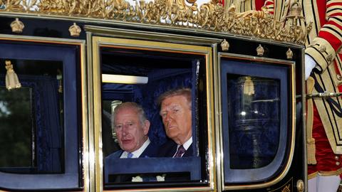 US-Präsident Donald Trump und der britische König Charles schauen aus einer goldenen Kutsche heraus in die Kamera.