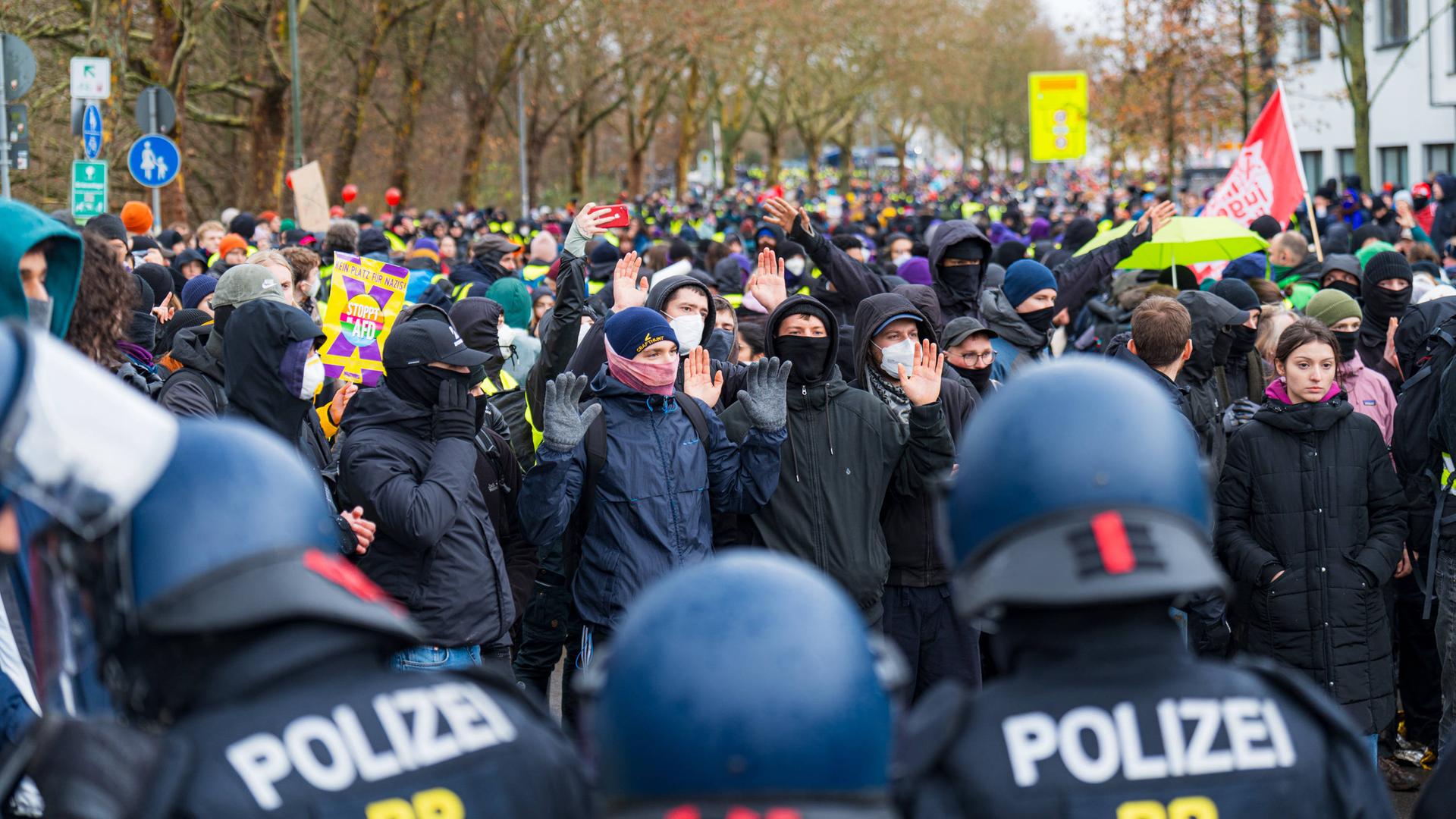 Proteste und Polizeieinsatz in Gießen bei Gründung der AfD-Jugendorganisation. Im Vordergrund sind uniformierte Polizisten mit Helm zu sehen. Dann eine Vielzahl Demonstrierender mit und ohne Maske. Es sind Fahnen zu sehen. 