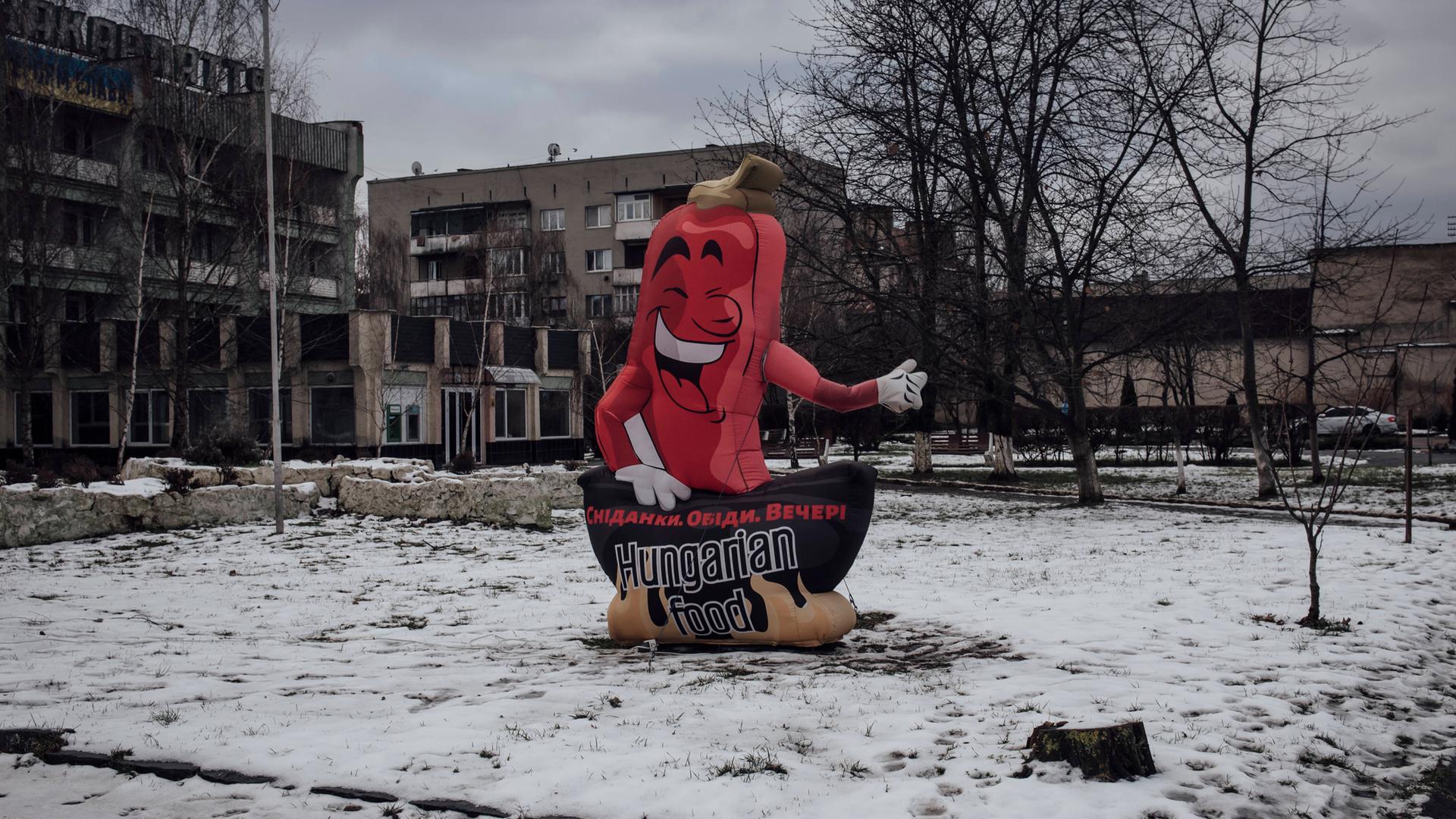 Ein Werbeaufsteller in Form einer roten Paprika mit der Aufschrift "Hungarian Food" steht auf einem leeren Platz.