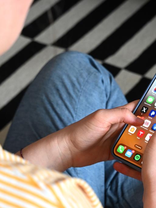 Eine Jugendliche sitzt auf dem Boden und nutzt ein Smartphone - auf dem Display sind verschiedene Apps zu sehen. Eine Jugendliche sitzt auf dem Boden und nutzt ein Smartphone - auf dem Display sind verschiedene Apps zu sehen.