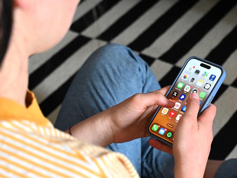 Eine Jugendliche sitzt auf dem Boden und nutzt ein Smartphone - auf dem Display sind verschiedene Apps zu sehen. Eine Jugendliche sitzt auf dem Boden und nutzt ein Smartphone - auf dem Display sind verschiedene Apps zu sehen.