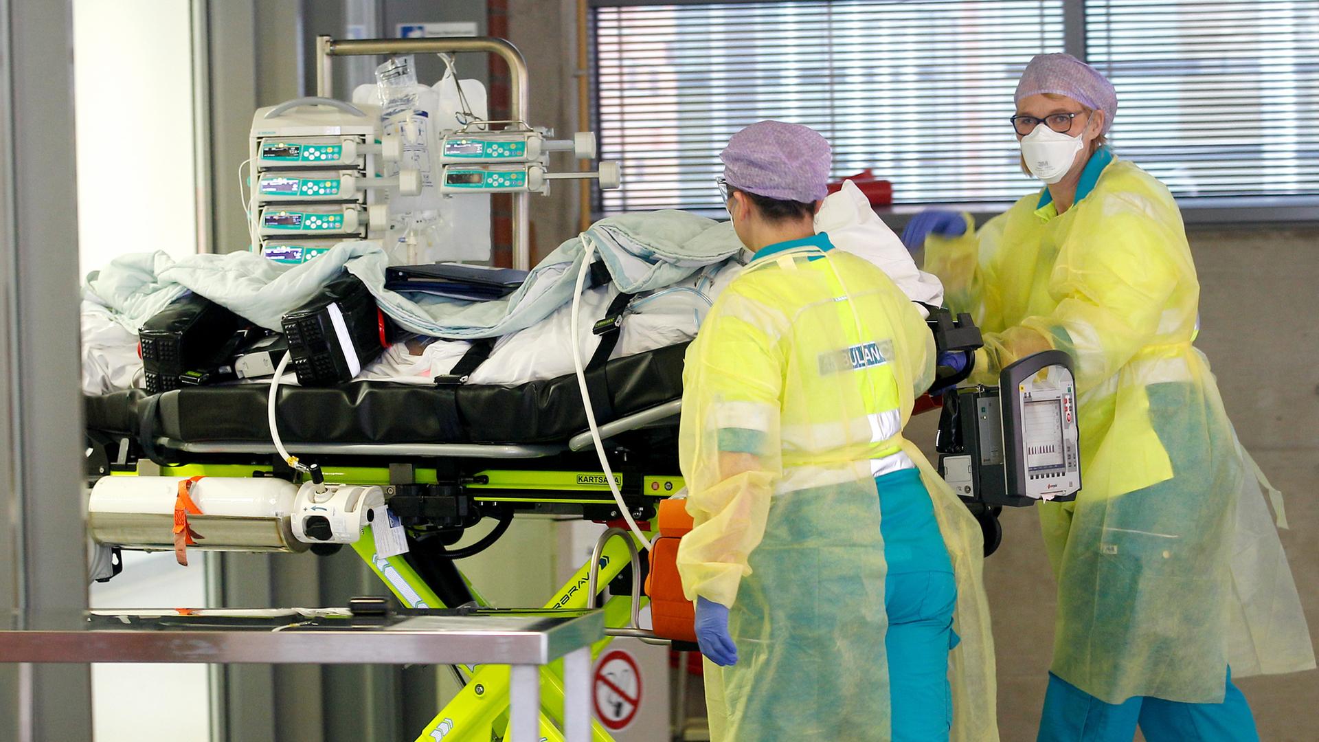 Krankenhauspersonal in Schutzanzügen und mit Mund-Nasenschutz schiebt einen Patienten auf einer Trage. Krankenhauspersonal in Schutzanzügen und mit Mund-Nasenschutz schiebt einen Patienten auf einer Trage.