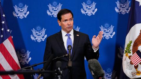 Rubio steht vor einem Mikrofon und spricht. Er gestikuliert mit einer Hand. Im Hintergrund sind US-Flaggen zu erkennen.