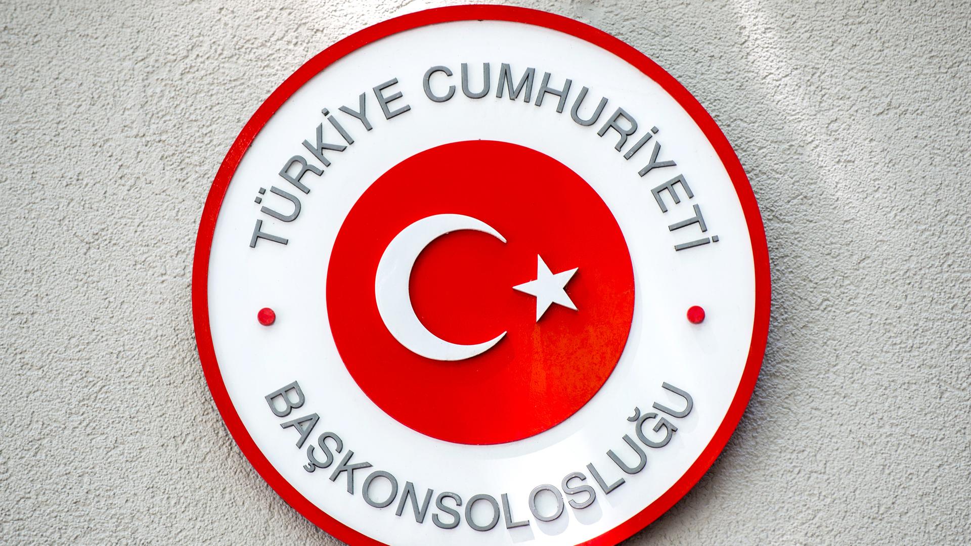 Das runde rot-weiße Schild mit türkischer Schrift und Halbmond mit Stern auf einer weißen Wand mit Rauhputz.