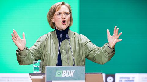 Brantner in einer olivgrünen Jacke steht am Rednerpult vor einer grünen LED-Wand, spricht und gestikuliert mit beiden Händen. 