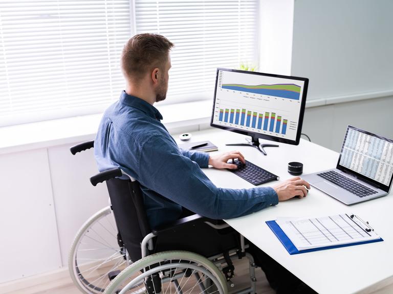 Ein Mann sitzt im Rollstuhl an seinem Büroarbeitsplatz.