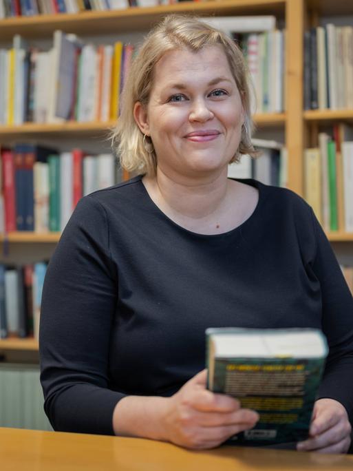 Die Schriftstellerin Berit Glanz sitzt im Literaturhaus Schleswig-Holstein in Kiel vor einem Bücherregal und lächelt in die Kamera.