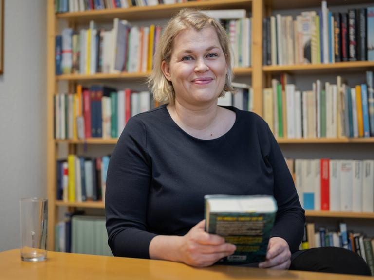 Die Schriftstellerin Berit Glanz sitzt im Literaturhaus Schleswig-Holstein in Kiel vor einem Bücherregal und lächelt in die Kamera.