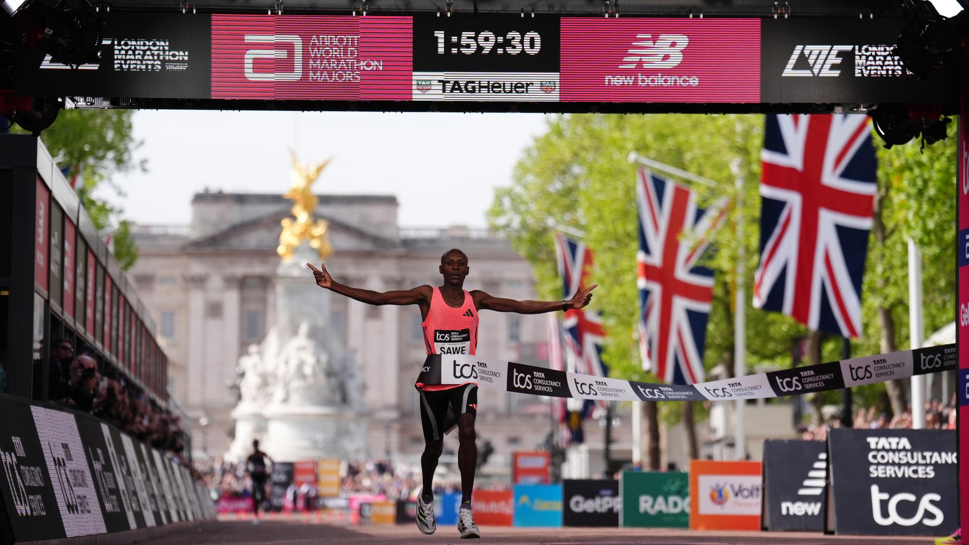 Der Kenianer Sabastian Sawe läuft ins Ziel. Über ihm zeigt eine Uhr die neue Weltrekordzeit von 1 Stunde, 59 Minuten und 30 Sekunden
