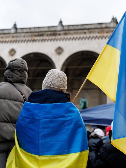 Teilnehmende einer Solidaritätsdemo mit der Ukraine demonstrieren mit ukrainischen Flaggenauf dem Odeonsplatz in München.