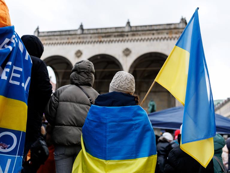 Teilnehmende einer Solidaritätsdemo mit der Ukraine demonstrieren mit ukrainischen Flaggenauf dem Odeonsplatz in München.