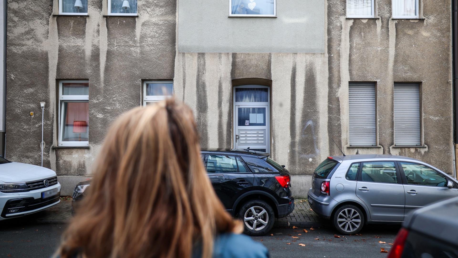 Eine Frau steht vor einem Mehrfamilienhaus.